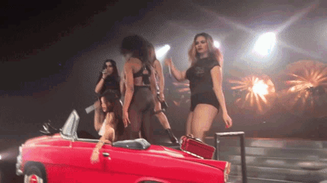 a group of women are standing around a red car