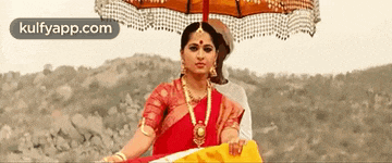 a woman in a red saree is holding an umbrella over her head
