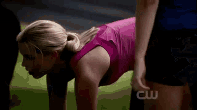 a woman in a pink tank top is doing push ups with a cw logo behind her