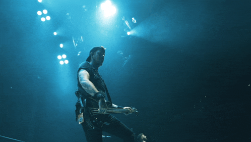 a man playing a bass guitar on a stage with blue lights