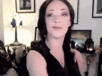 a woman in a black dress is standing in a living room with a lamp .