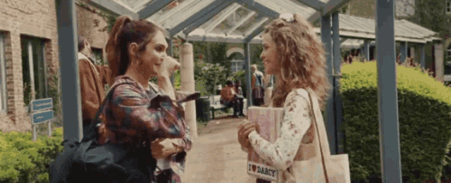 two women are standing next to each other and one of them has a bag that says i love darcy