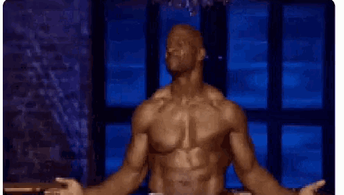 a shirtless man is standing with his arms outstretched in front of a window in a dark room .