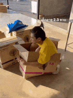 a man in a yellow shirt is sitting in a cardboard box that says sharp