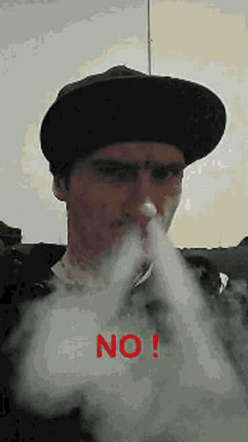 a man wearing a hat is blowing smoke out of his nose with the word no in red