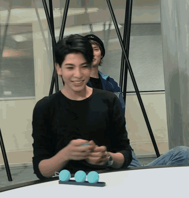 a man in a black shirt is sitting at a table with three blue balls on it
