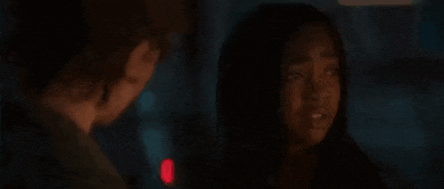 a young man with curly hair is standing in a dark room looking at something .