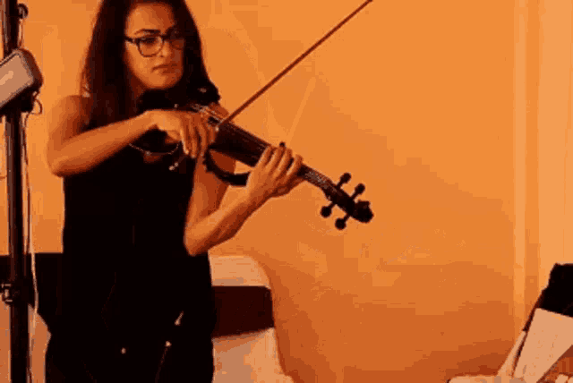 a woman is playing a violin in front of an orange wall