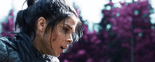 a close up of a woman 's face with purple flowers in the background and a ponytail .