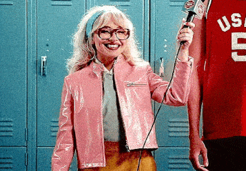 a woman in a pink jacket is holding a microphone in front of a man in a red shirt .
