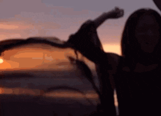 a silhouette of a woman standing in front of a sunset with her arms outstretched .