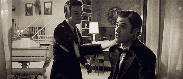 two men in suits and bow ties are standing in a living room