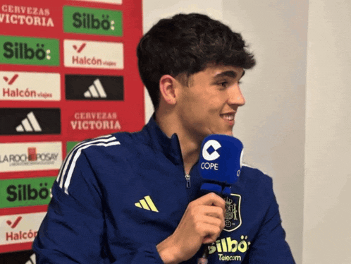 a young man wearing a blue adidas jacket is talking into a cope microphone