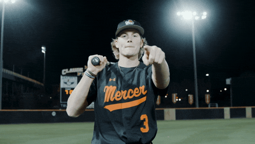 a baseball player wearing a black mercer jersey points at the camera