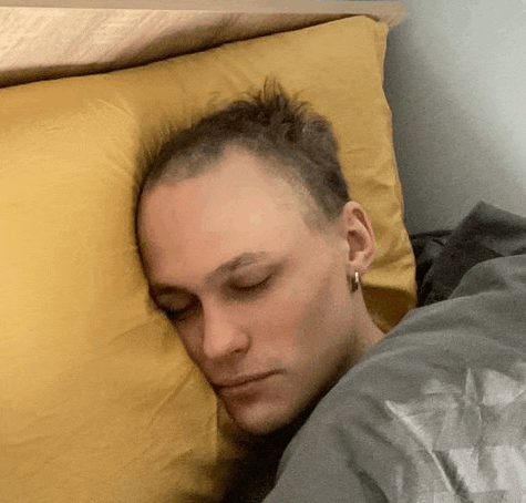a man with a mohawk is sleeping on a bed with a yellow pillow .