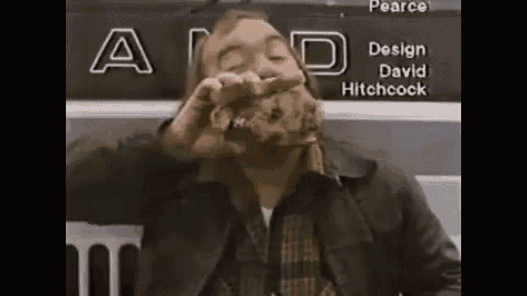a man with a beard is eating a piece of meat while sitting in front of a sign that says a .