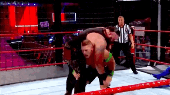 a wrestler is carrying another wrestler on his back in a wrestling ring while a referee watches .