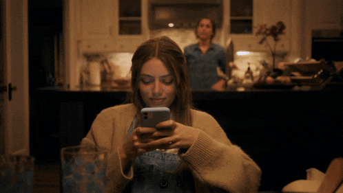 a woman is looking at her phone while another woman stands in the background