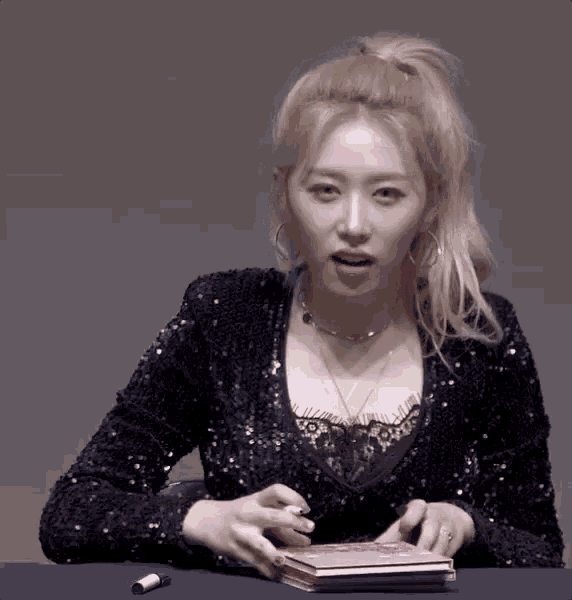 a woman in a black sequined top is sitting at a table holding a pink purse .