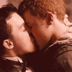 a man in a suit and tie kisses another man in a black jacket