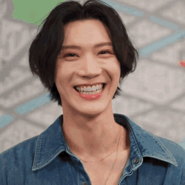 a close up of a young man wearing a denim shirt and a necklace smiling .