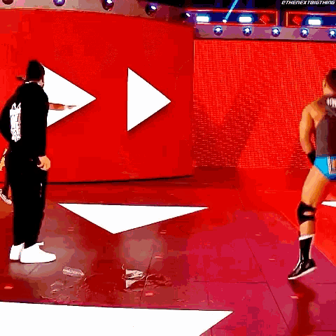 two wrestlers are standing in front of a red wall with arrows pointing in opposite directions ..