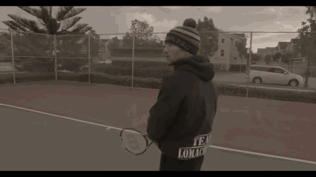 a man holding a tennis racquet on a tennis court wearing a beanie with the word box on it