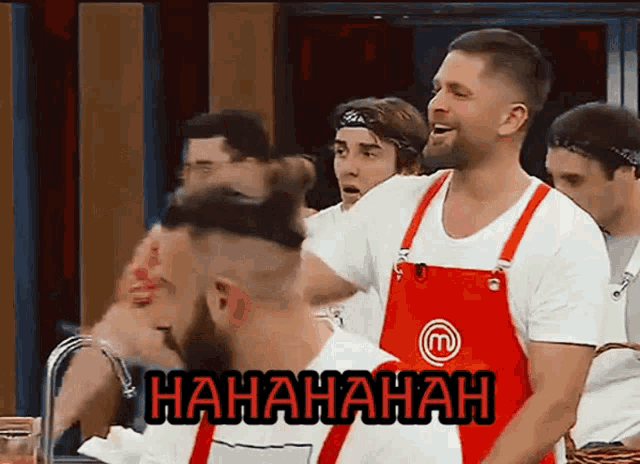 a group of men are laughing and one of them is wearing a red apron with a m on it