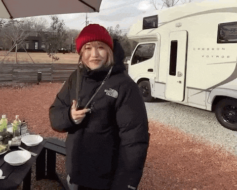 a woman in a black jacket and red hat is standing in front of a rv .