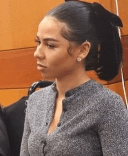 a woman in a grey sweater and earrings is sitting in a courtroom .