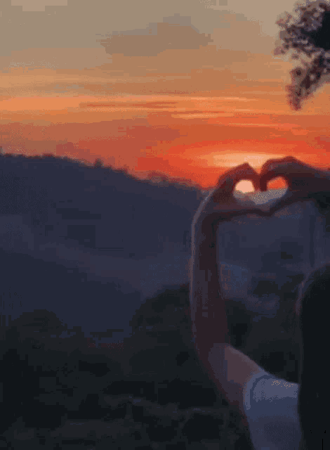 a person making a heart shape with their hands against a sunset