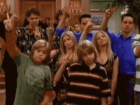 a group of people are standing in a room with their hands in the air and making peace signs .