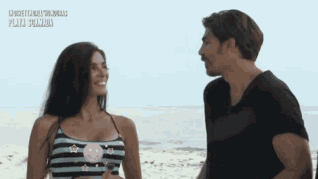 a man and a woman are standing on a beach and the woman is wearing a striped top with a smiley face on it