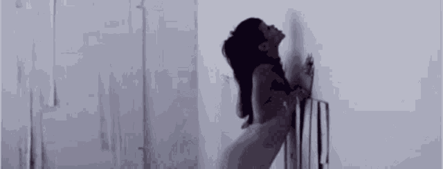 a naked woman is leaning against a wall in a dark room .