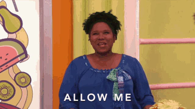 a woman in a blue shirt stands in front of a sign that says " allow me "