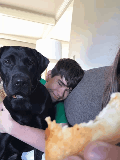 a boy laying on a couch with a black dog and a piece of bread