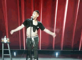 a man singing into a microphone with his arms outstretched in front of a red curtain