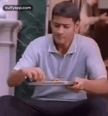 a man in a blue shirt is sitting on the floor eating food from a plate .
