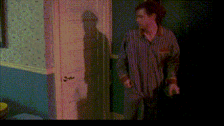 a man in a striped shirt opens a door with his shadow on the wall