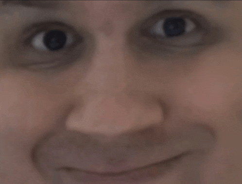 a close up of a man 's face with his eyes looking at the camera and smiling .
