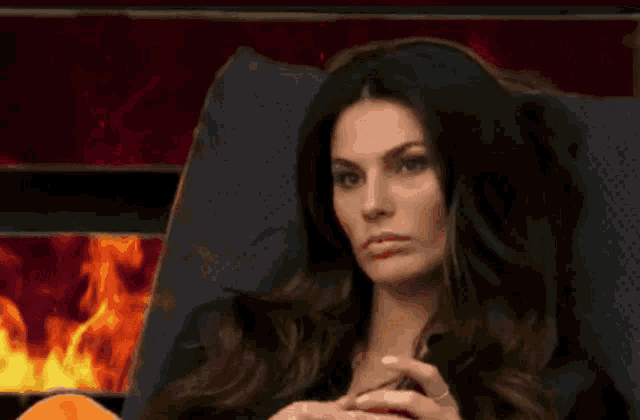 a woman is sitting in a chair with a fire in the background behind her