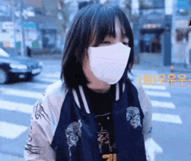 a woman wearing a mask and a jacket is standing on the street .