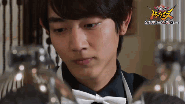 a man in an apron and bow tie looks at a glass with a sign that says 3/6
