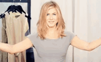 a woman is standing in a room with her arms outstretched in front of clothes hanging on a rack .