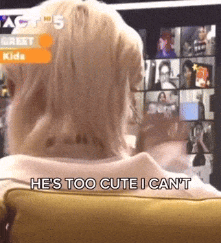 a woman is sitting in front of a screen with the words he 's too cute i can 't