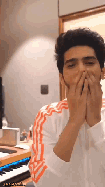 a man is covering his mouth with his hands in front of a piano keyboard