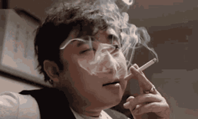 a man in a suit is smoking a cigarette with smoke coming out of his mouth