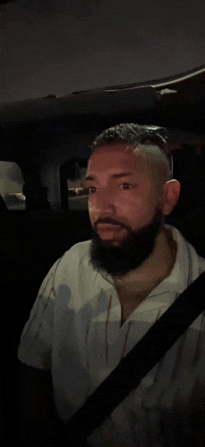 a man with a beard is smiling while sitting in a car at night