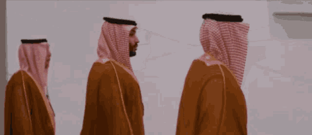 three men wearing traditional arabic clothing are walking in a line