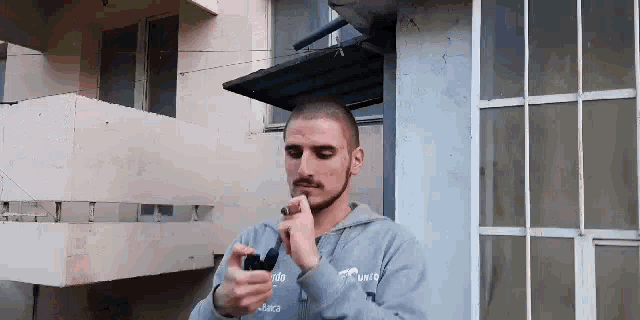 a man with a beard is smoking a cigarette in front of a building